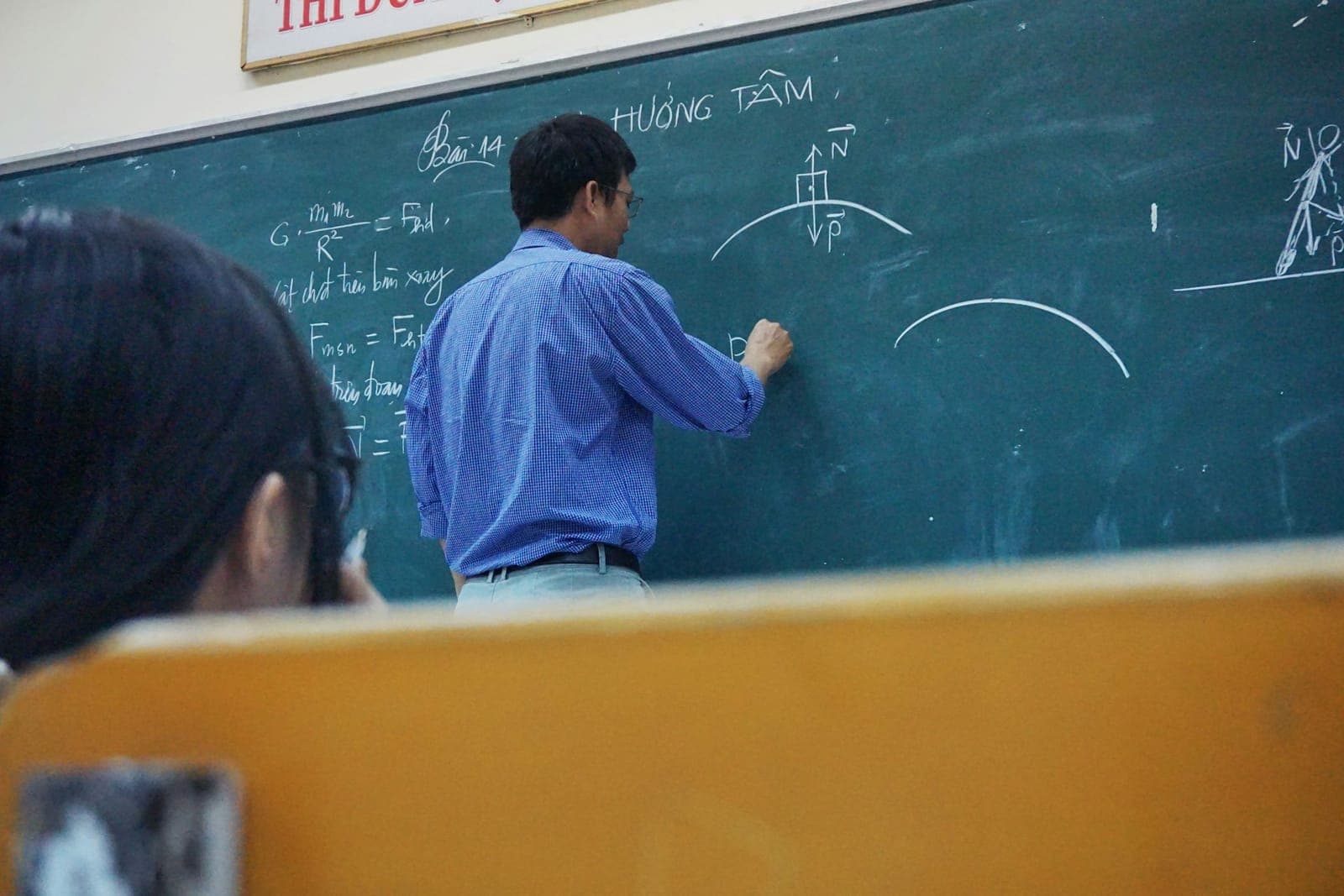 Yeşil tahtaya fizik denklemleri yazan öğretmen, arkadan