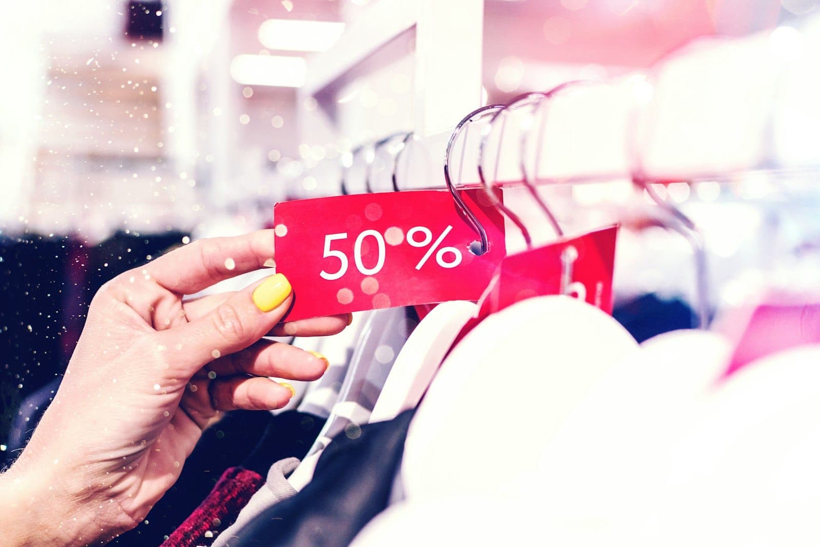 Askıdaki giysiden sarkan kırmızı %50 indirim etiketini tutan el